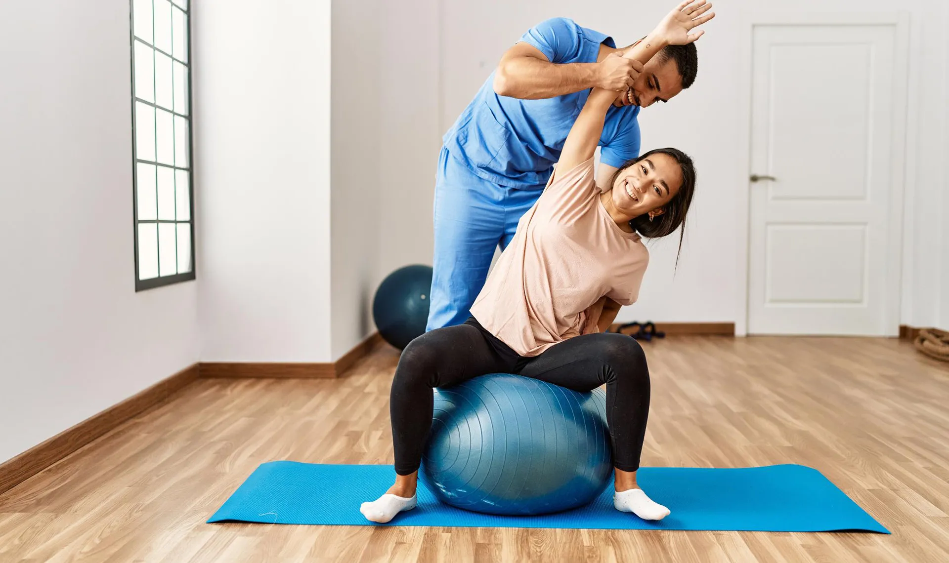 Bewegungstherapie im Reha-Zentrum St. Radegund – Physiotherapeut unterstützt Patientin bei Dehnübung auf Gymnastikball